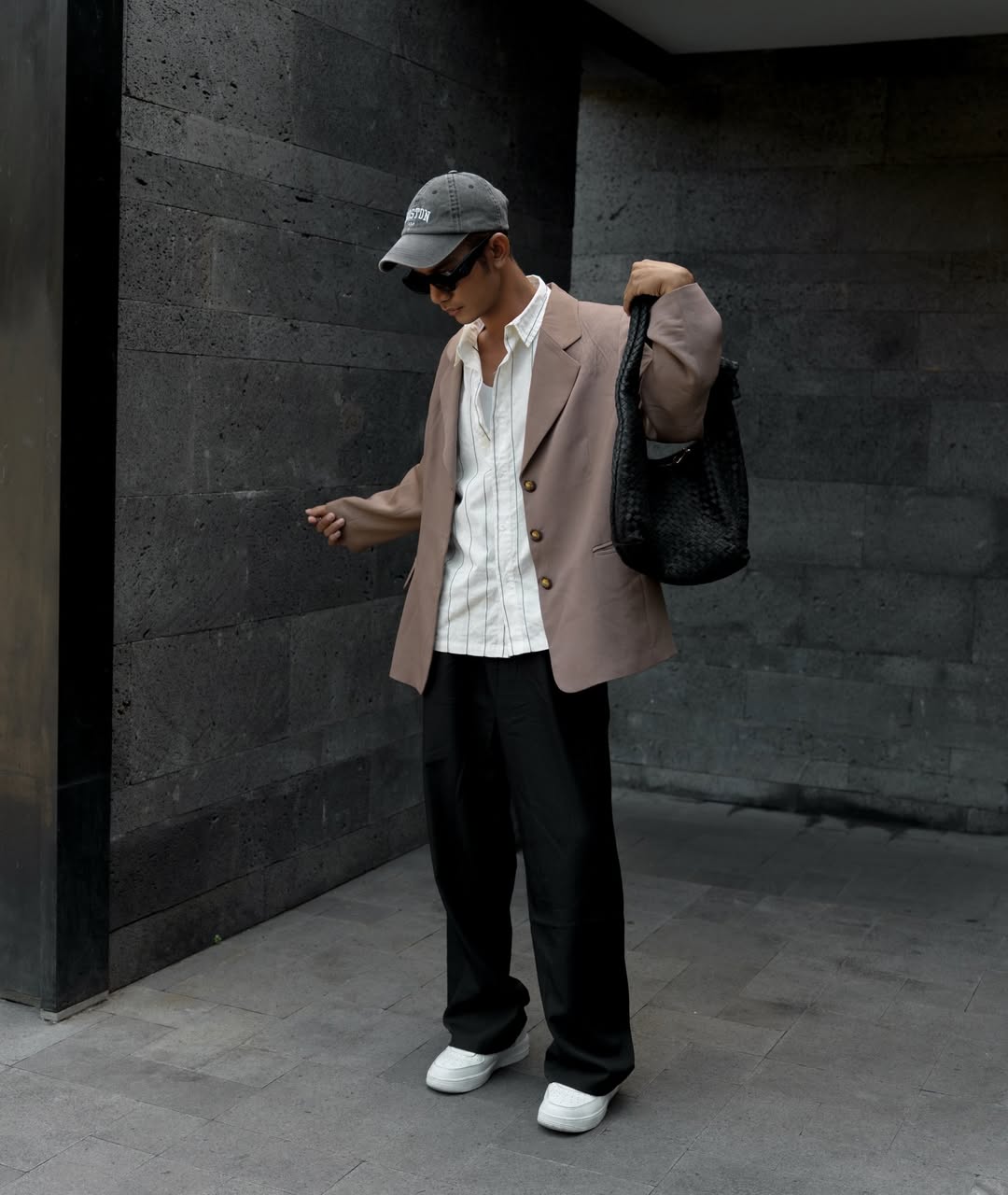 Person wearing a beige blazer, white shirt, black pants, and cap, holding a black bag handcrafted leather