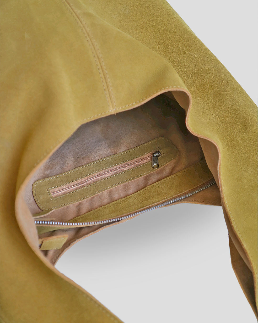 Close-up of a brown suede shoulder bag with a zipper pocket